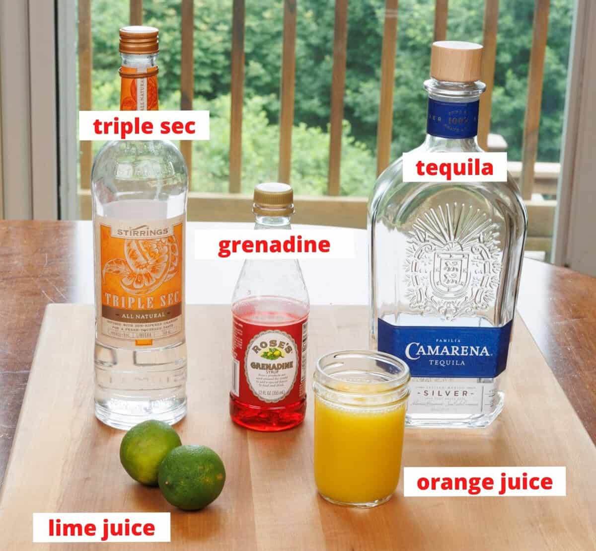 ingredients in a tequila sunrise cocktail on a wooden cutting board in a kitchen.
