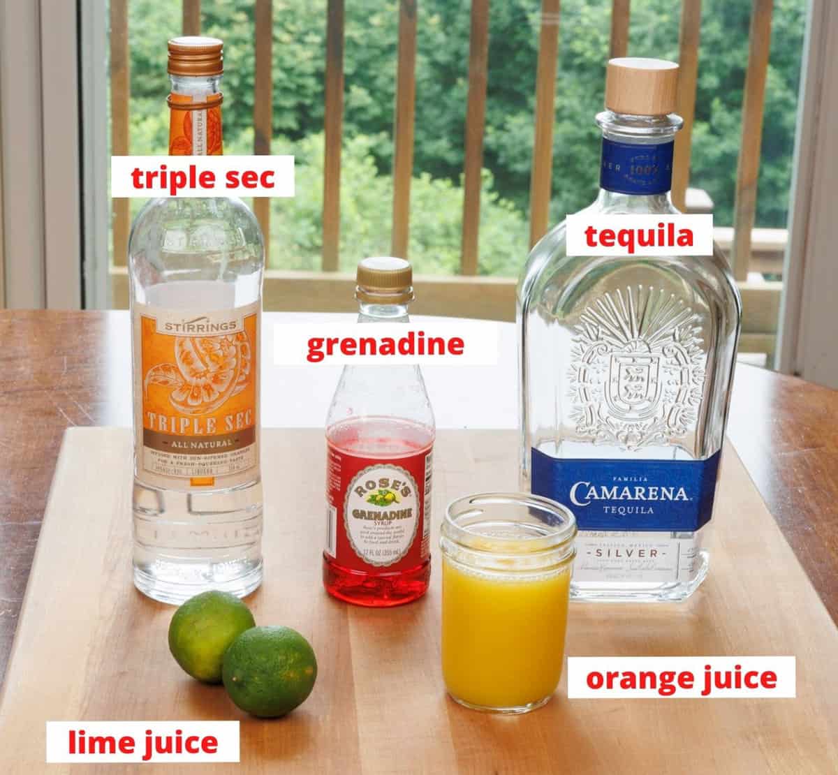 ingredients in a tequila sunrise cocktail on a wooden cutting board in a kitchen