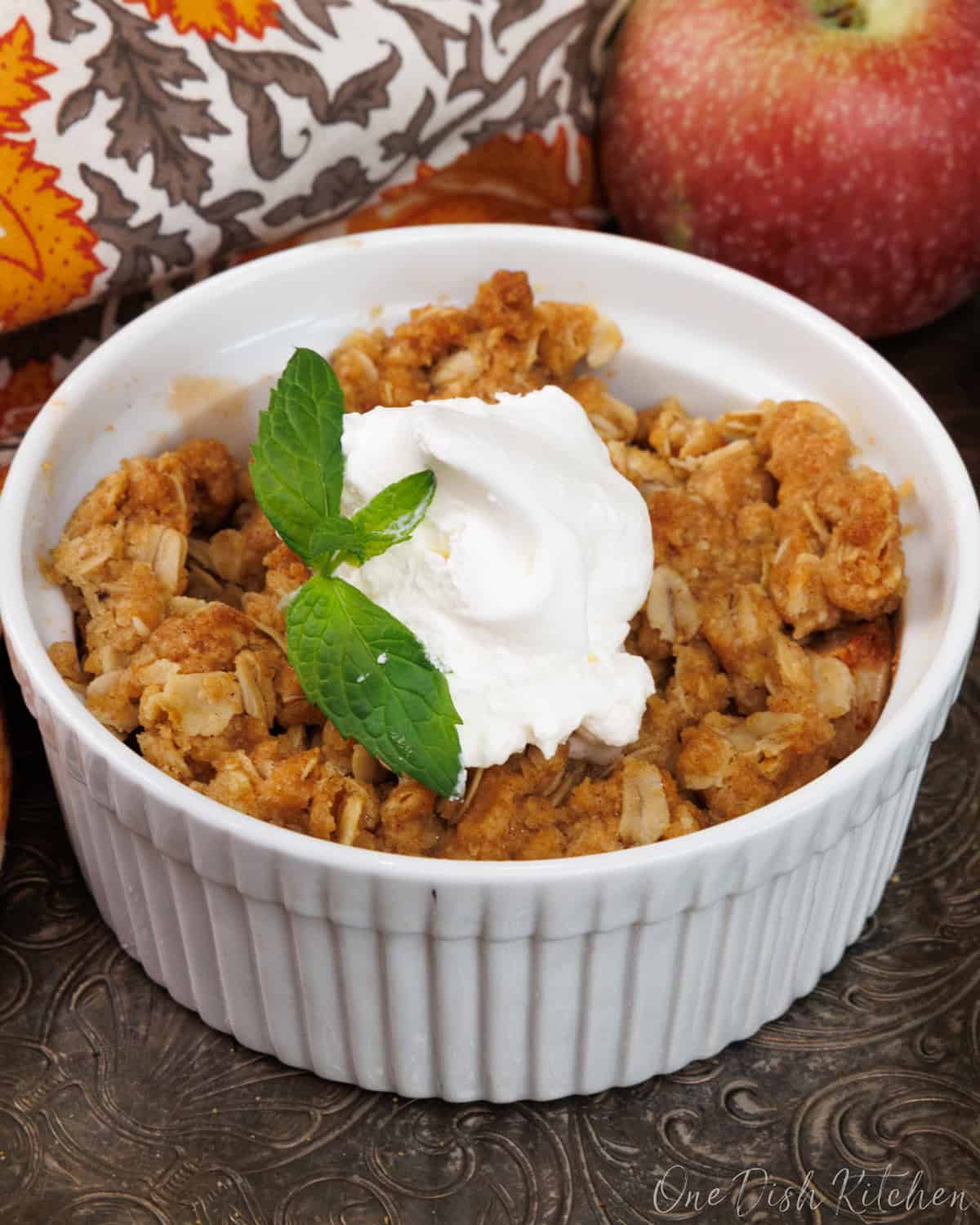 one small apple crisp in a white ramekin on a silver tray.