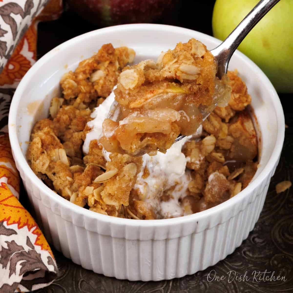 a small apple crisp topped with ice cream in a ramekin.