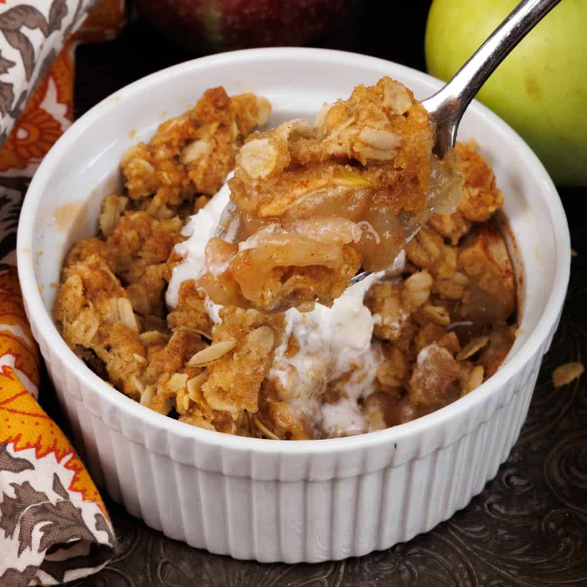 a spoon in an individual apple crisp with apples hanging off of the spoon.