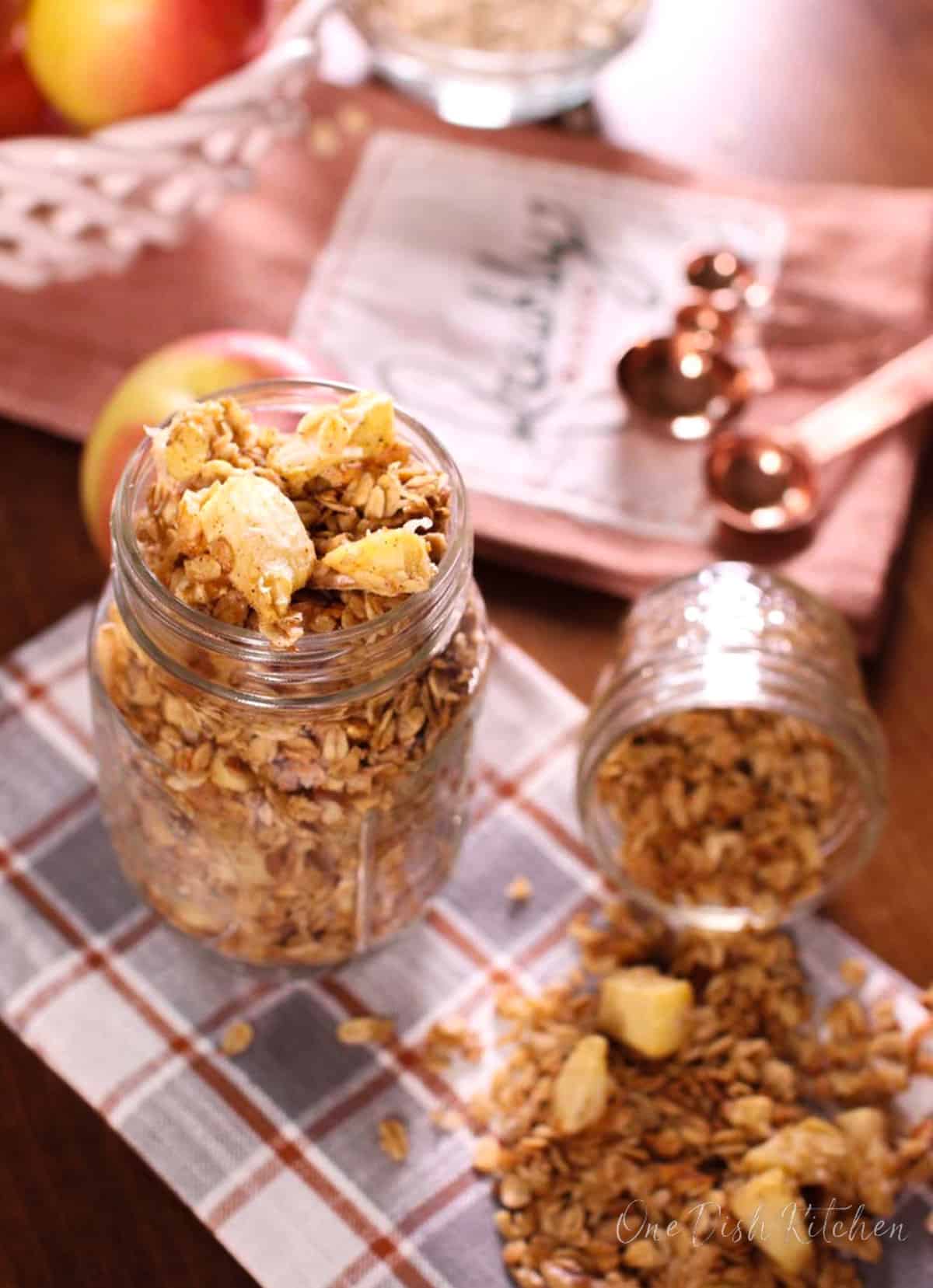a mason jar filled with granola and apples next to measuring spoons and a red napkin.