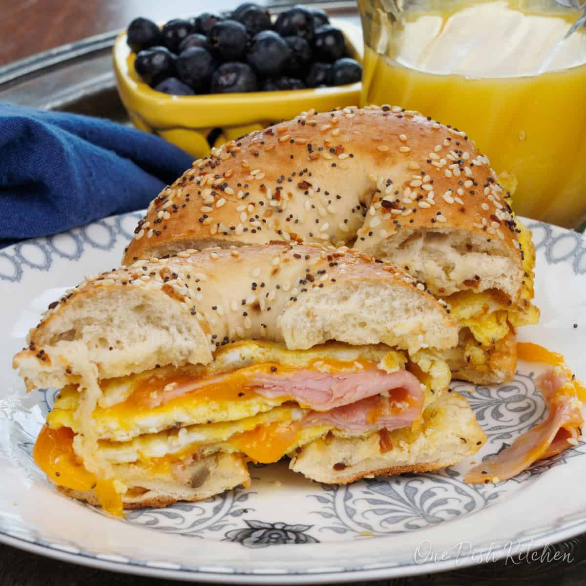 a ham and cheese breakfast bagel sliced in half on a plate.