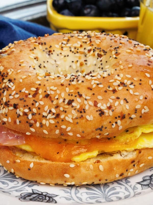 a breakfast bagel with ham and cheese on a blue plate next to a glass of orange juice.