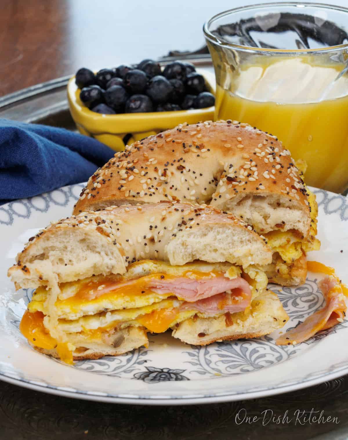 a ham and cheese breakfast bagel sliced in half on a plate.