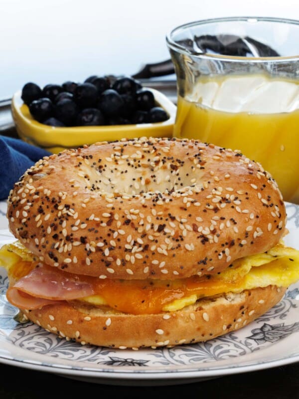 a breakfast bagel with ham and cheese on a blue plate next to a glass of orange juice