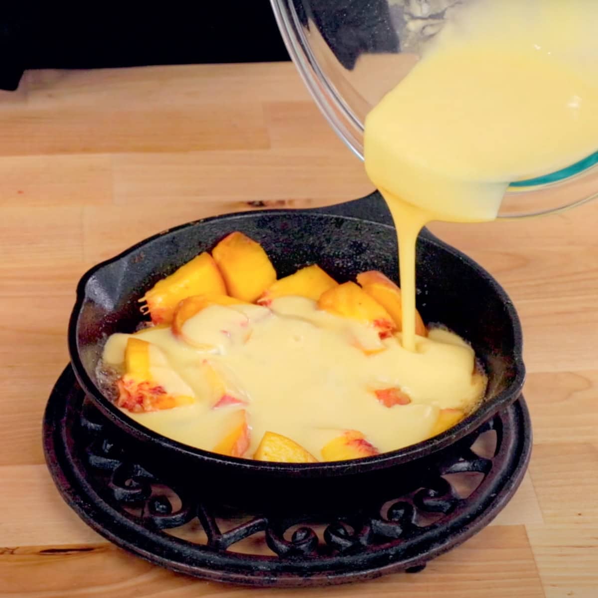 dutch baby batter poured over one slice fresh peach in a small cast iron skillet.