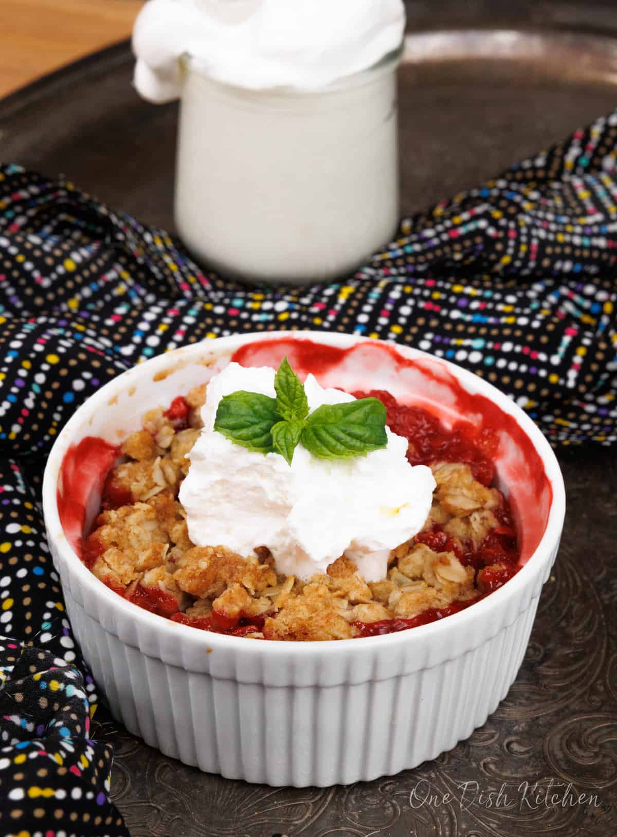 a mini strawberry crisp topped with whipped cream and a spring of fresh mint on a silver tray