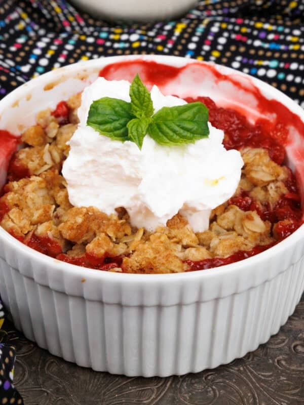 a mini strawberry crisp topped with whipped cream and a spring of fresh mint on a silver tray.
