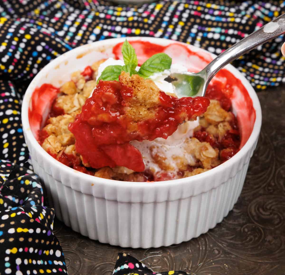 an individual strawberry crisp with a spoon on the side of the dish.