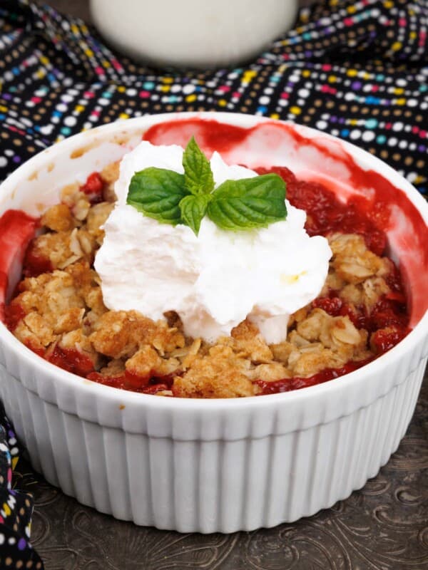 a mini strawberry crisp topped with whipped cream and a spring of fresh mint on a silver tray