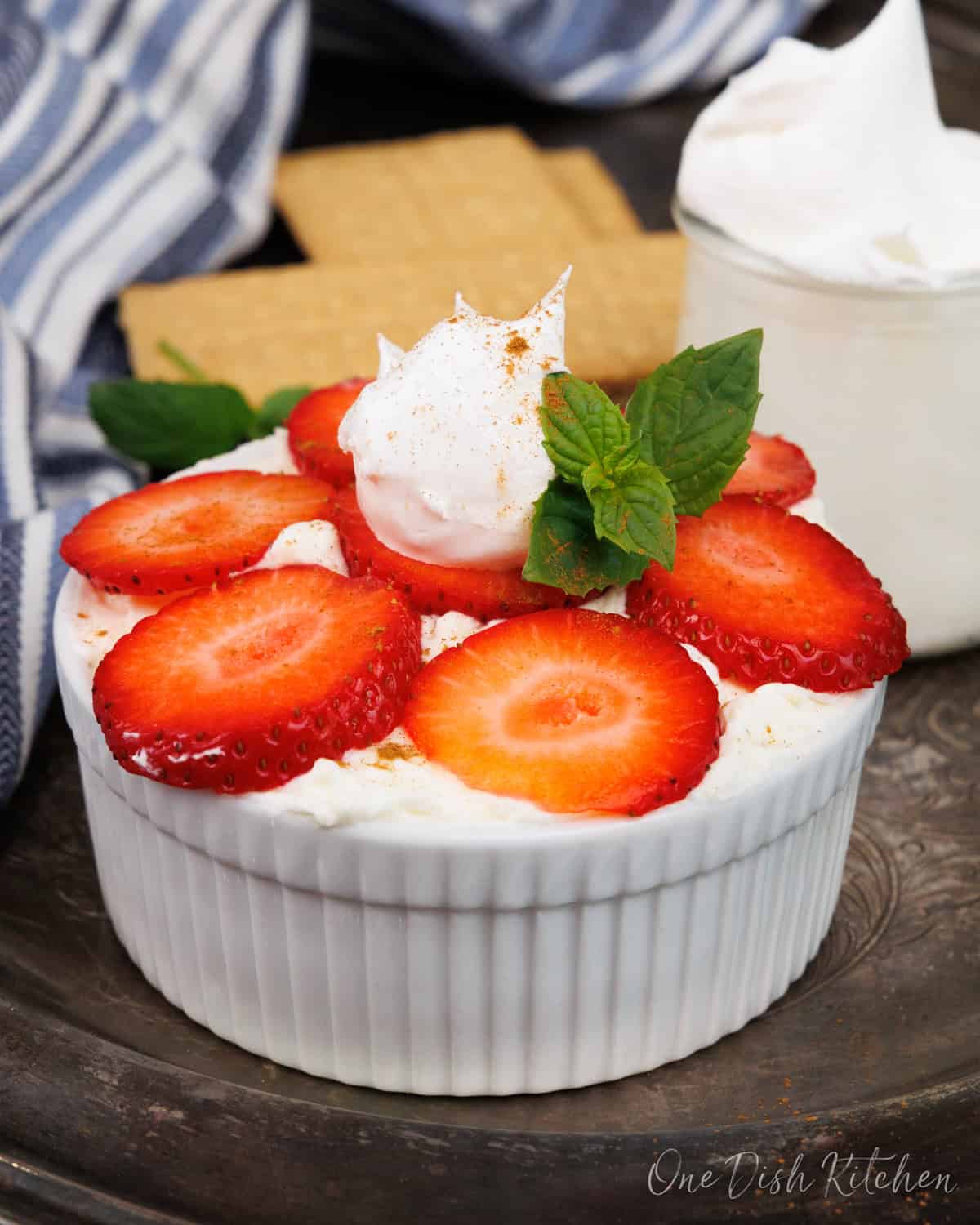 a mini strawberry icebox cake topped with strawberries next to a blue towel and a jar of whipped cream.