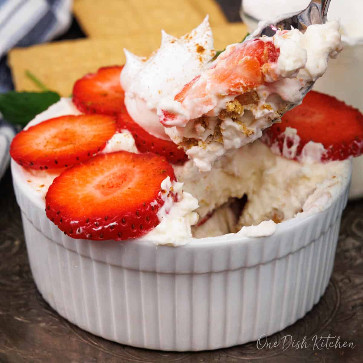 a strawberry icebox cake in a small ramekin with a spoon on the side.
