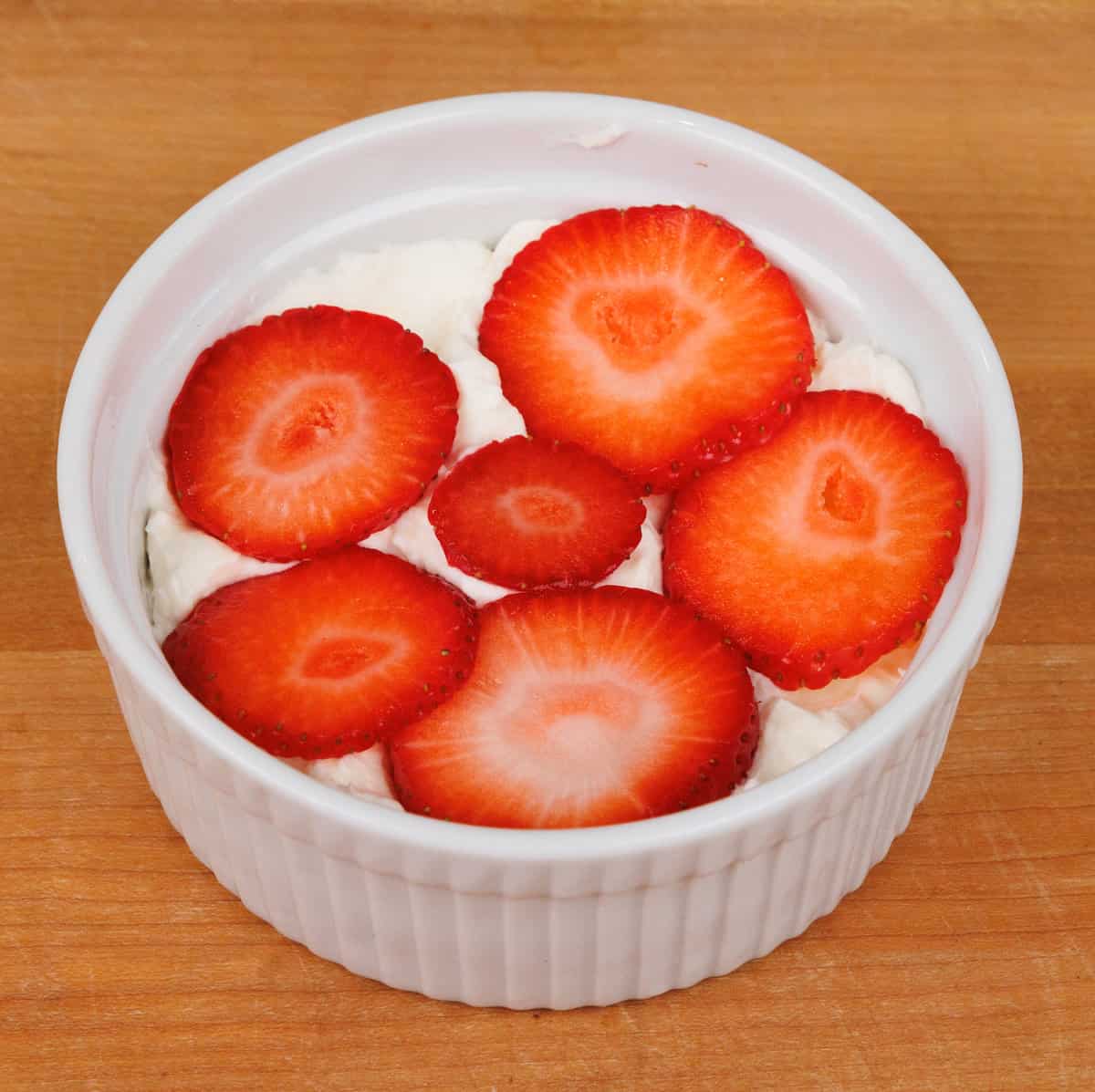 a layer of sliced strawberries over whipped cream and graham crackers in a small dish.