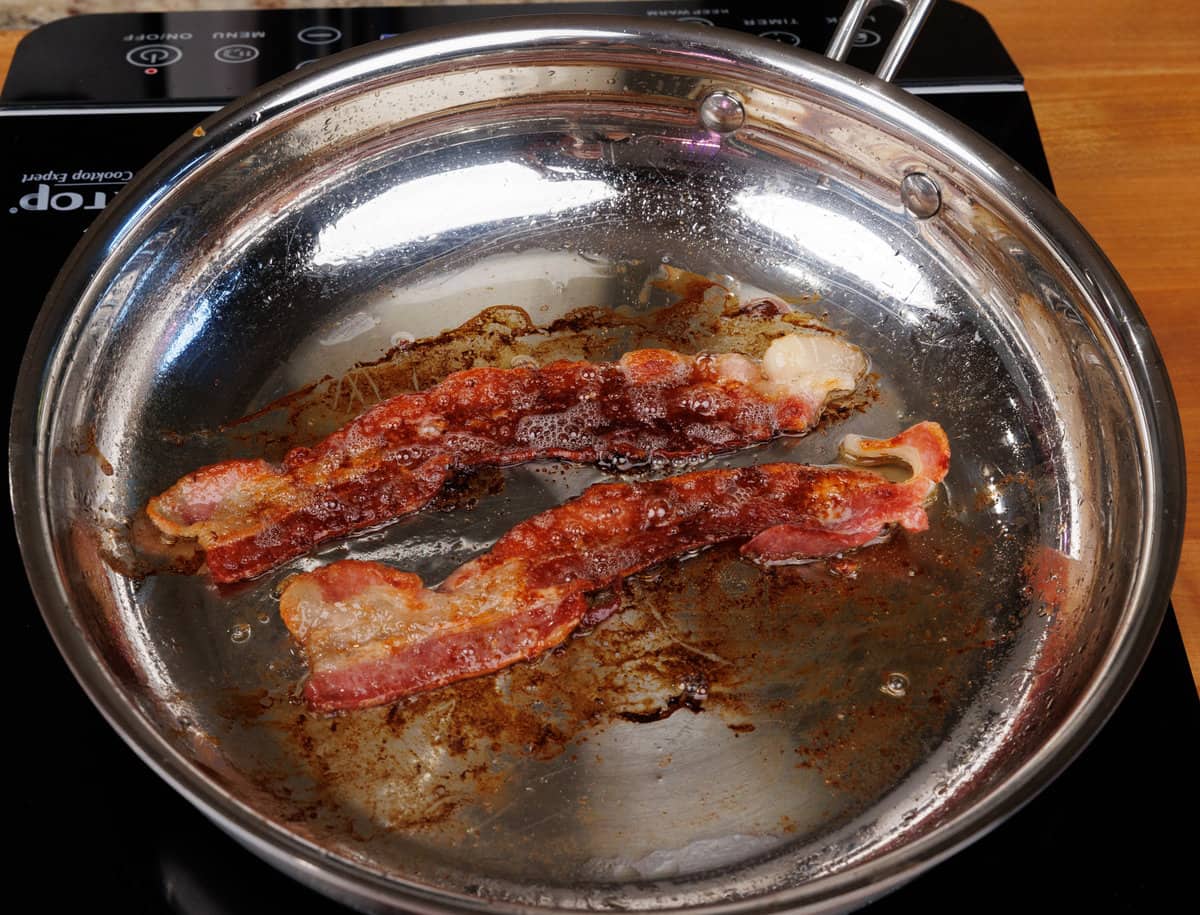 two strips of bacon frying in a skillet