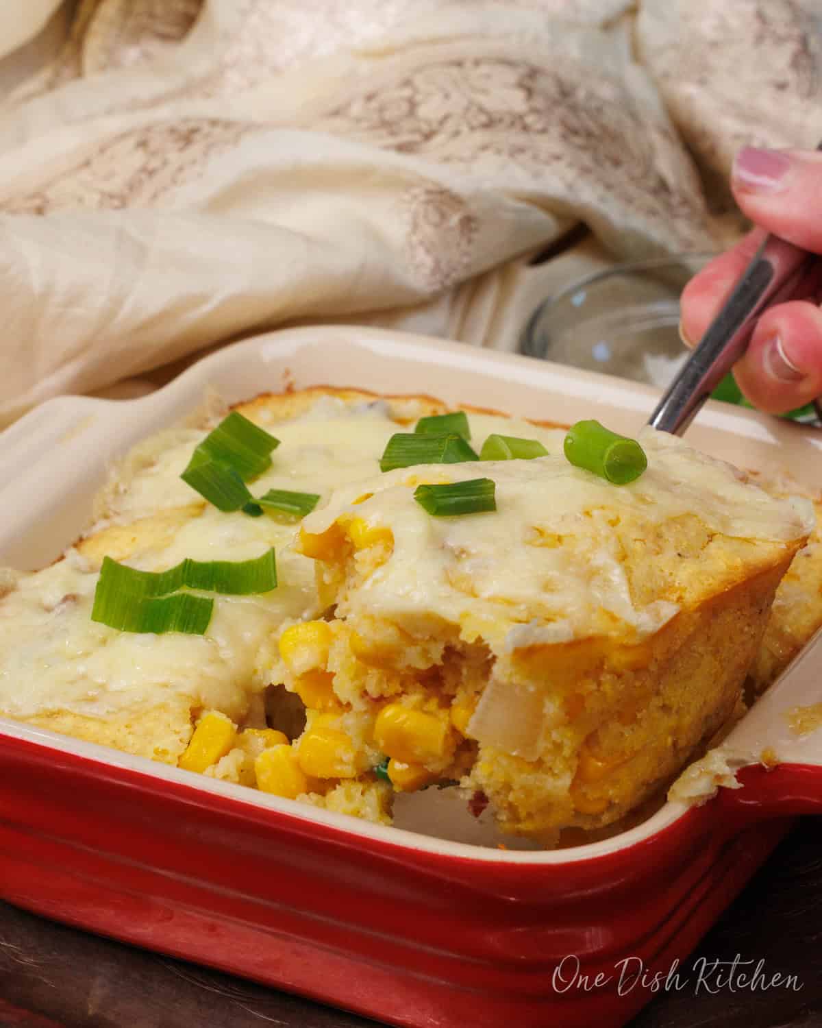 a small corn casserole in a red baking dish with a scoop being taken out.