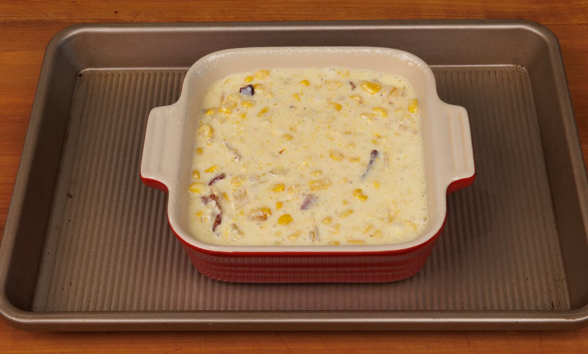 corn casserole batter in a small baking dish on a baking sheet