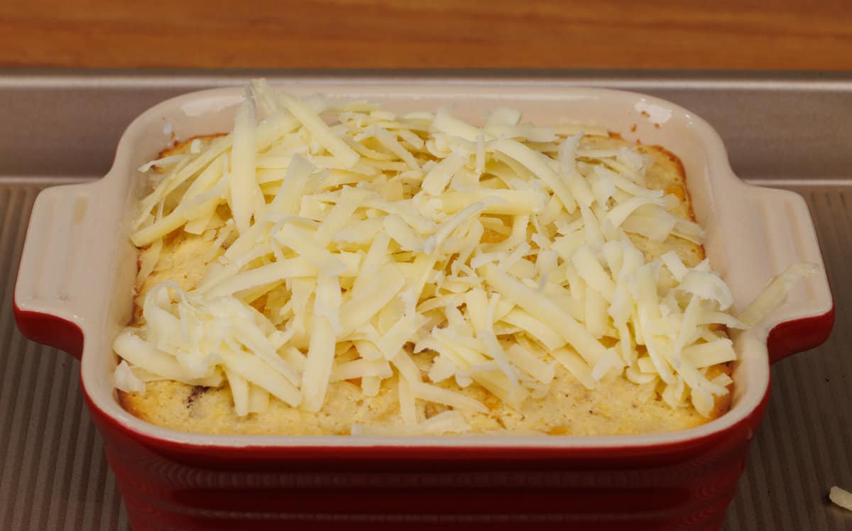 baked corn casserole topped with shredded cheese in a baking dish