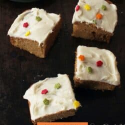 four pumpkin bars with cream cheese frosting on a black table.