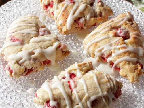 four strawberry scones topped with a glaze on a white plate