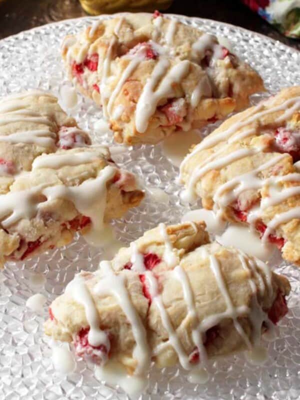 four strawberry scones topped with a glaze on a white plate