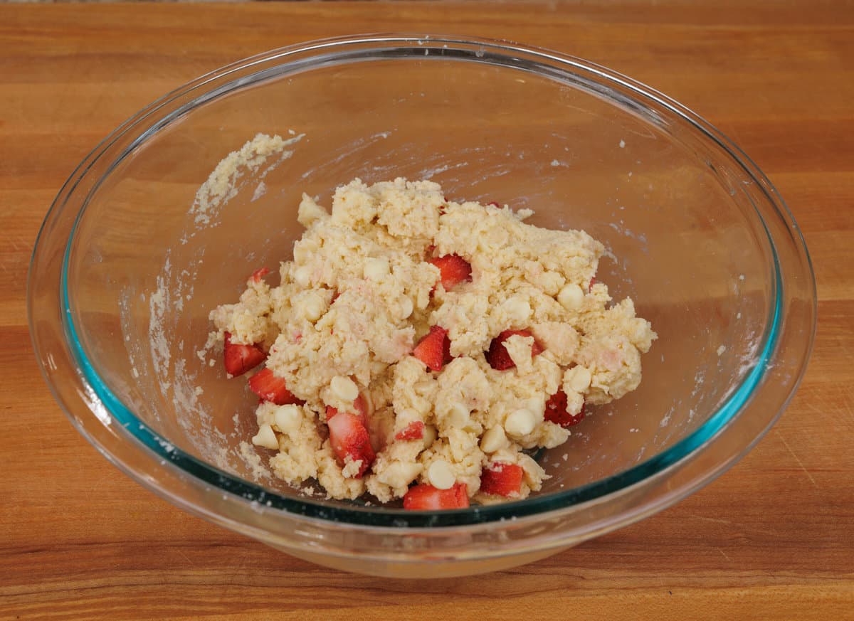 glass mixing bowl containing the combined dry and wet ingredients with slices of strawberries added for the strawberry scones.