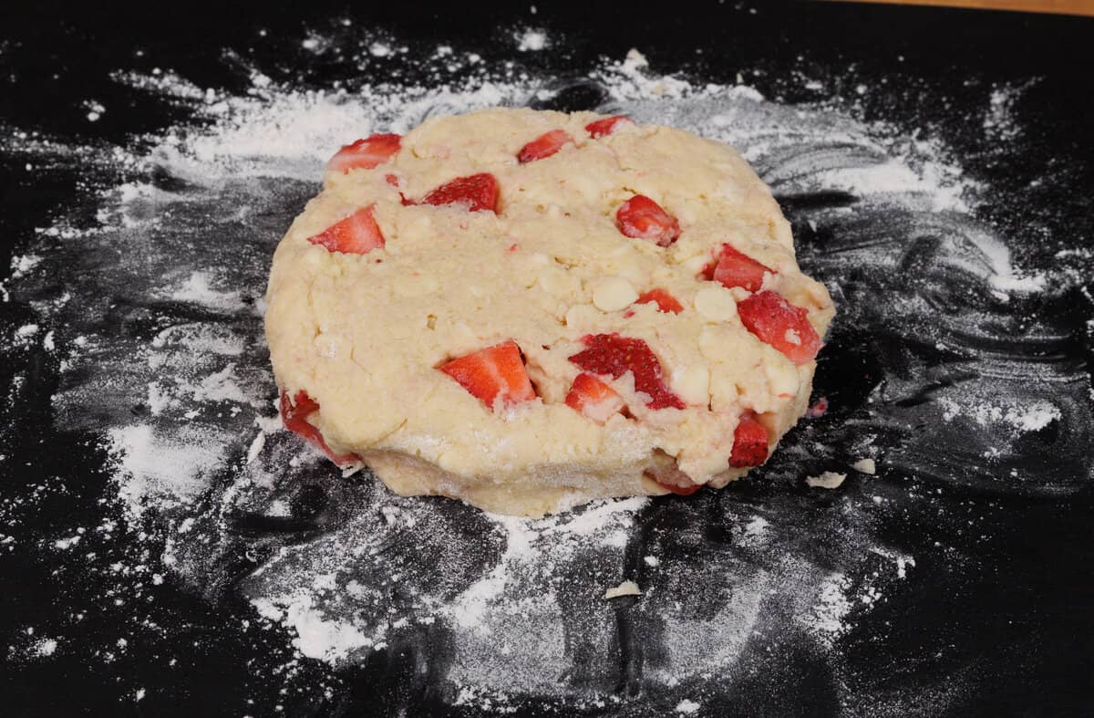 The strawberry scone dough shaped into a circle on a black cutting board.
