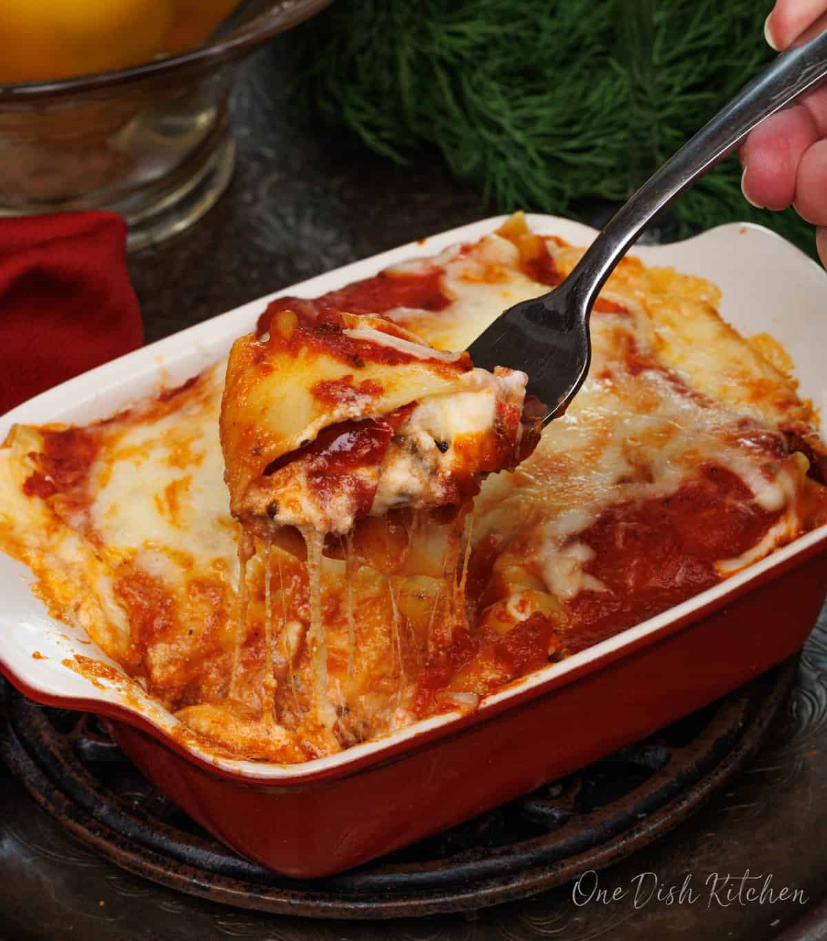 a fork filled with melted cheese, vegetables, and lasagna noodles next to a bunch of fresh parsley