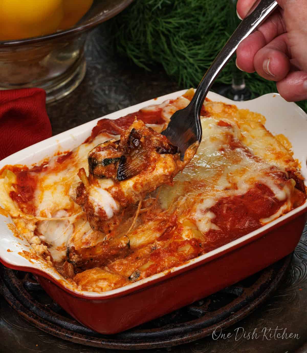A small vegetable lasagna on a silver tray next to a glass of wine, a fork and a red napkin