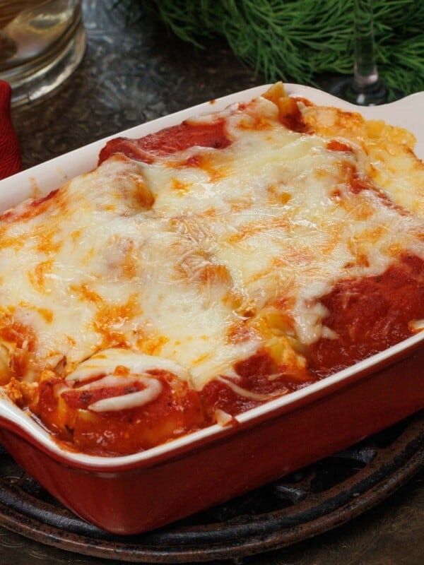 Vegetable lasagna in a small baking dish on a silver tray next to a glass of red wine