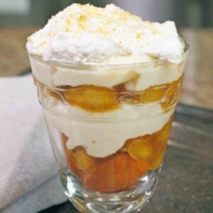 an old fashioned banana pudding made with caramelized bananas in a clear dessert glass next to a brown napkin.