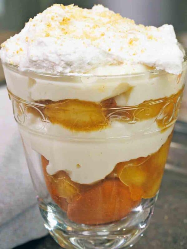 an old fashioned banana pudding made with caramelized bananas in a clear dessert glass next to a brown napkin.