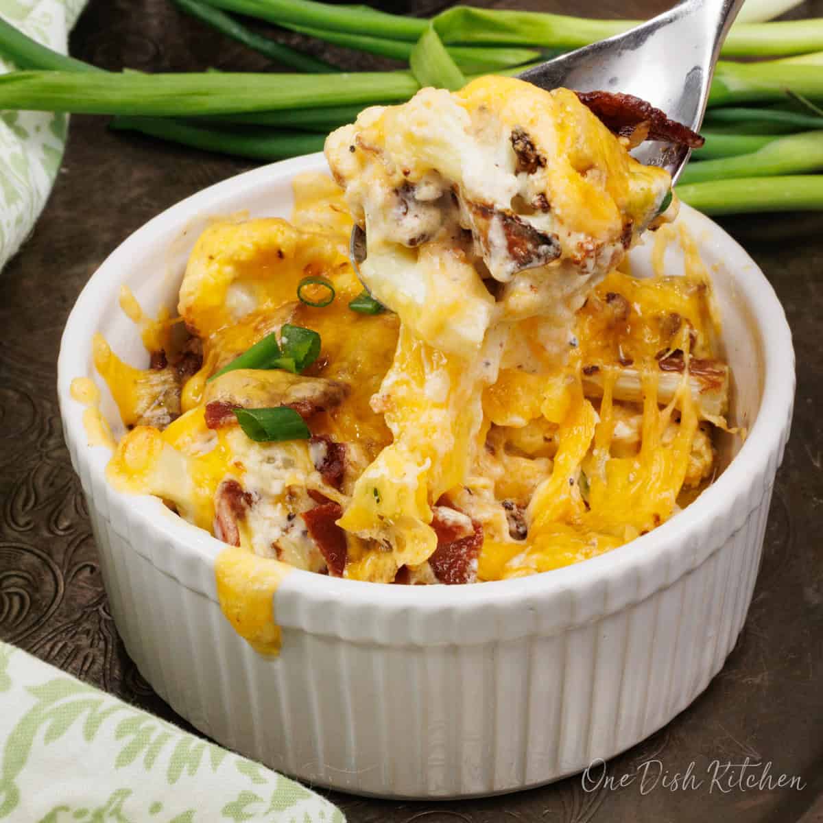 a single serving cauliflower casserole in a ramekin filled with roasted cauliflower, bacon, and cheese.