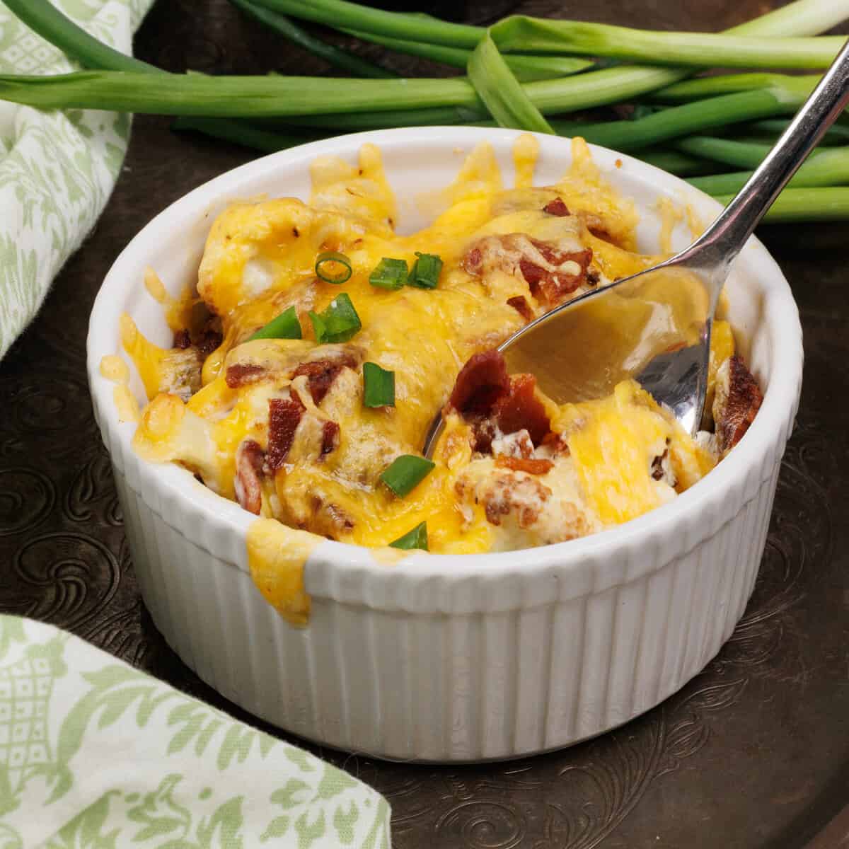 a small cauliflower casserole in a ramekin with a spoon scooping out bacon and cheese.