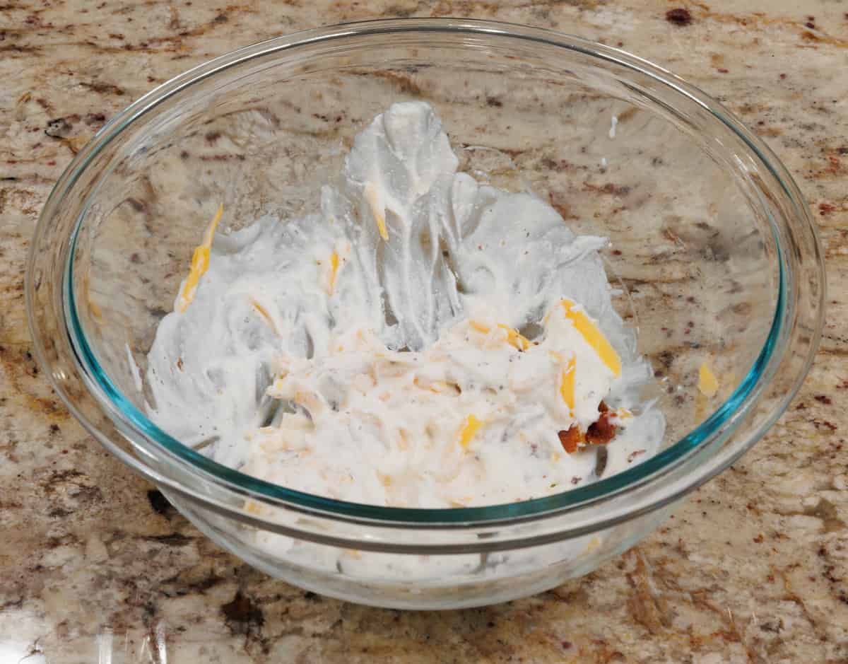 sour cream, heavy cream, cheese, and bacon in a mixing bowl on a kitchen counter