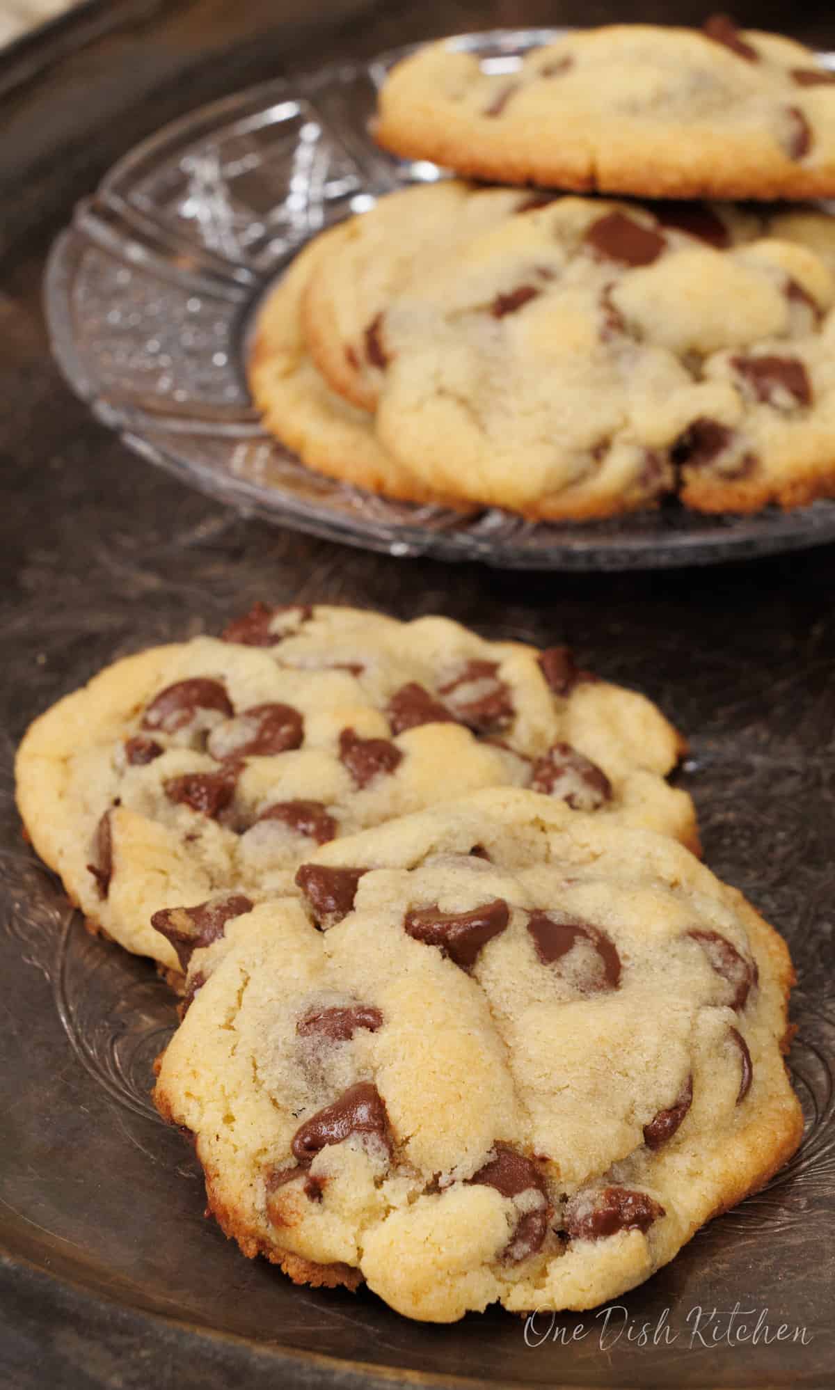 two chocolate chips on a silver tray next to a plate of two cookies