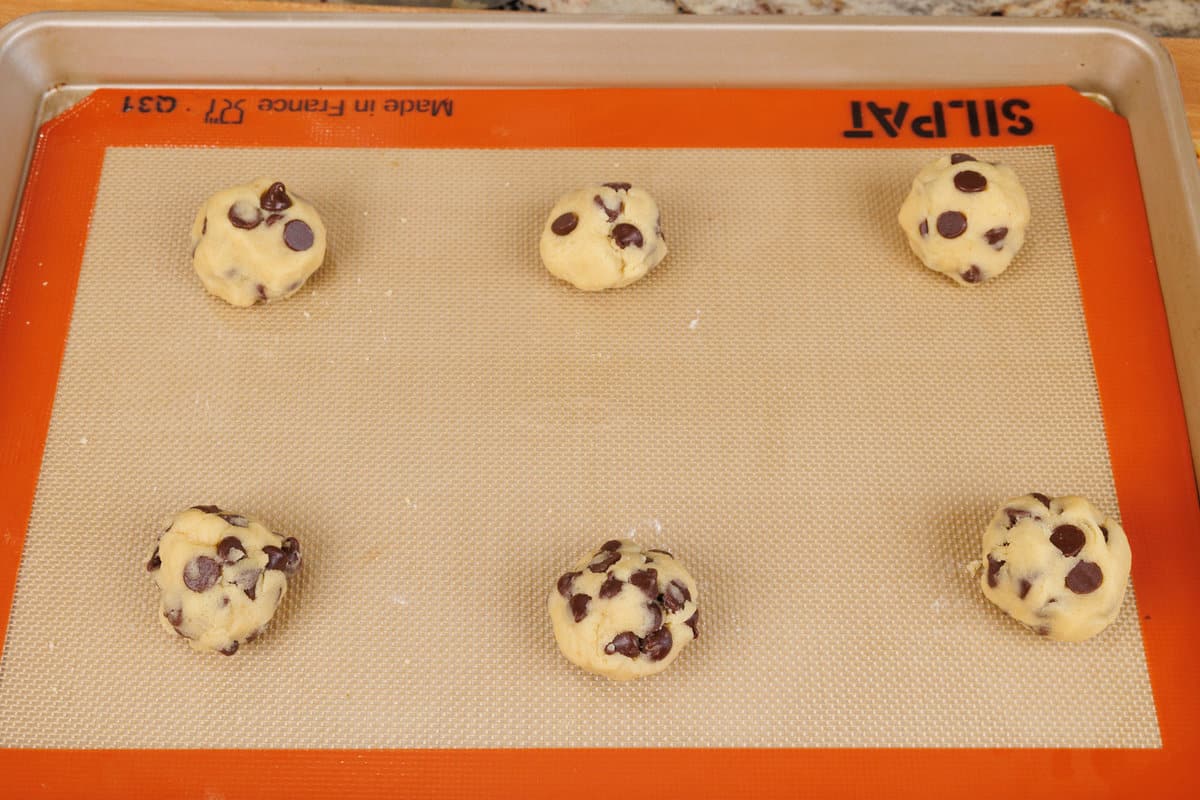 six balls of chocolate chip cookie dough on a baking sheet
