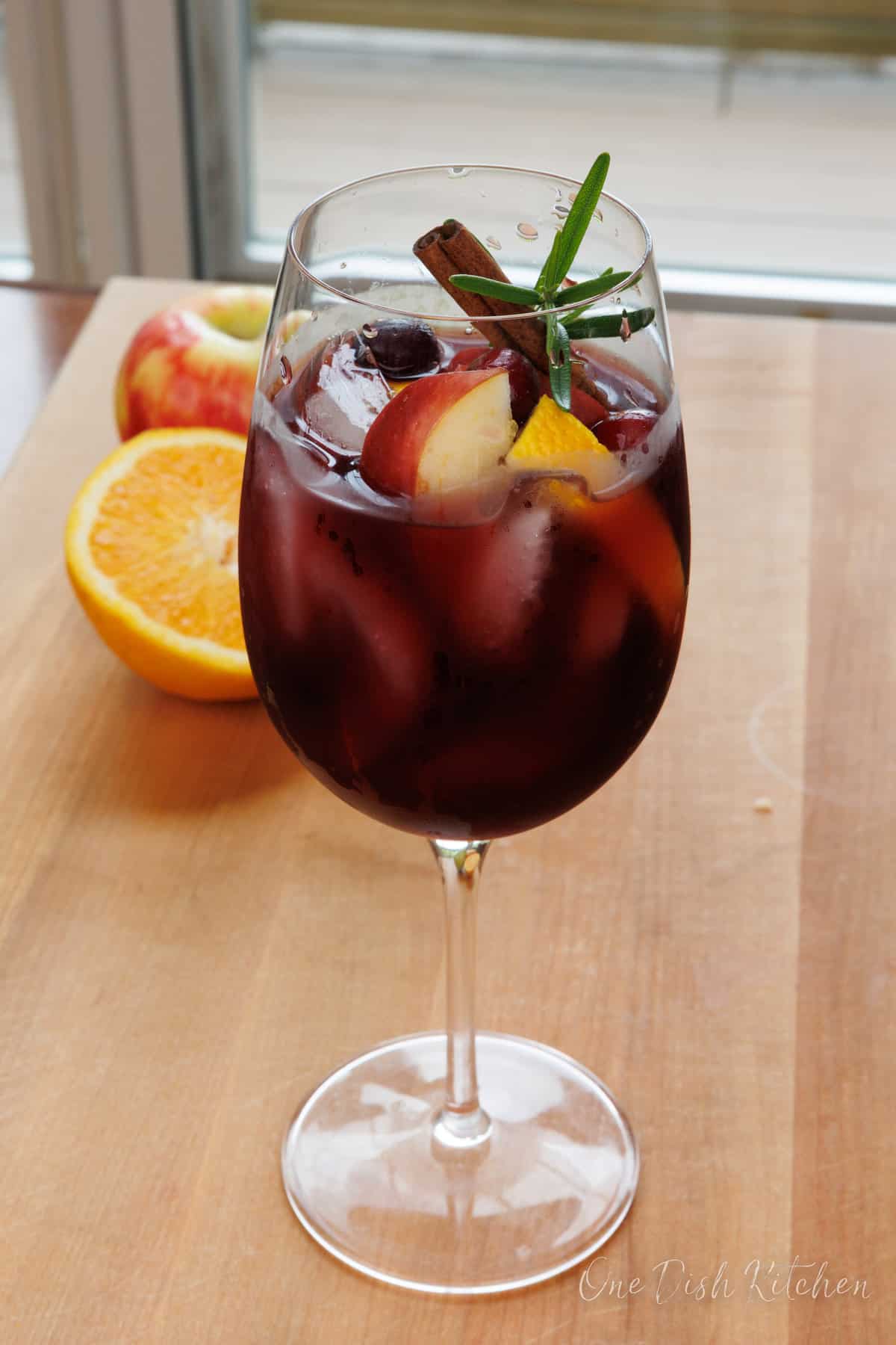a glass of fall sangria on a kitchen table next to orange slices and apple slices