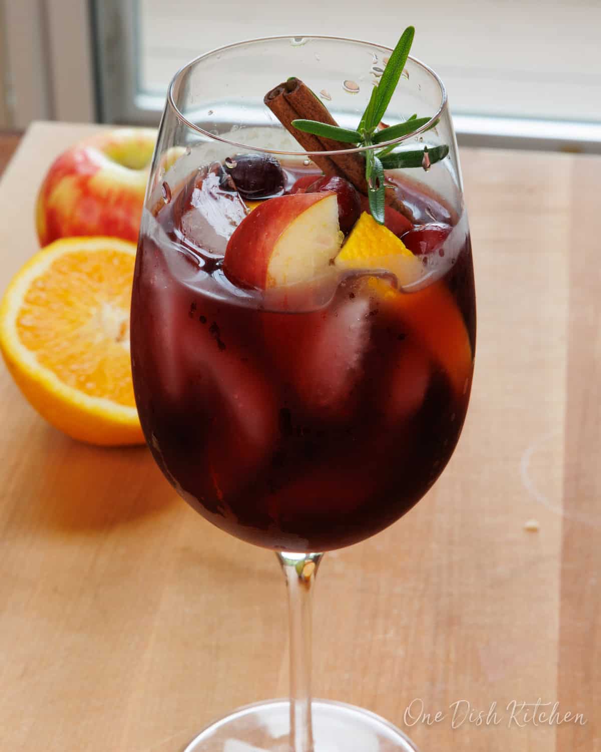 a single serving fall sangria in a glass garnished with fresh fruit and a cinnamon stick.