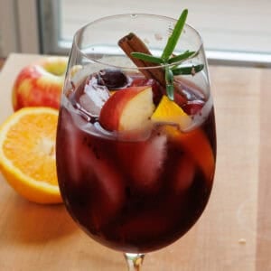 a single serving fall sangria in a glass garnished with fresh fruit and a cinnamon stick.