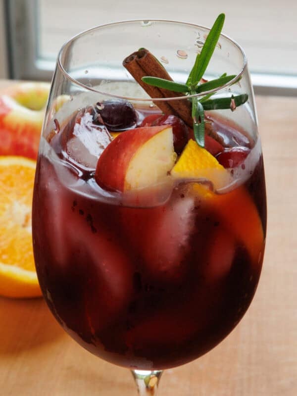 a single serving fall sangria in a glass garnished with fresh fruit and a cinnamon stick.