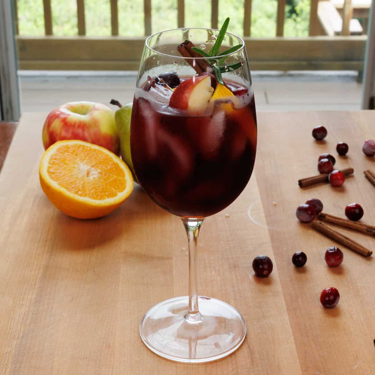 a fall sangria in a wine glass garnished with fresh rosemary, cranberries and orange slices