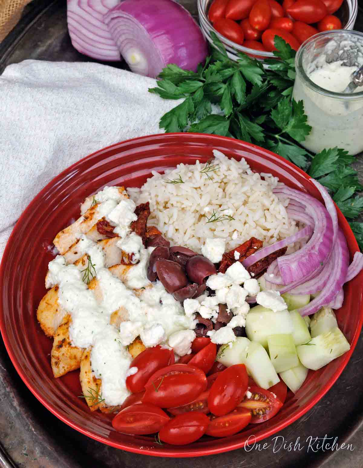 a greek chicken and rice bowl topped with tzatziki sauce on a silver tray next to a white napkin.