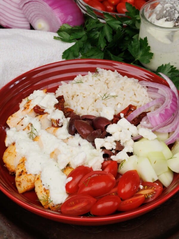 a greek chicken and rice bowl topped with tzatziki sauce on a silver tray next to a white napkin