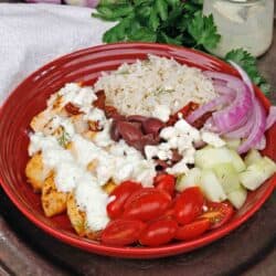 a greek chicken and rice bowl topped with tzatziki sauce on a silver tray next to a white napkin.