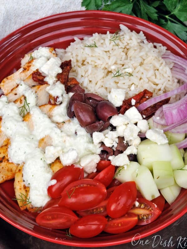 a greek chicken and rice bowl topped with tzatziki sauce on a silver tray next to a white napkin.