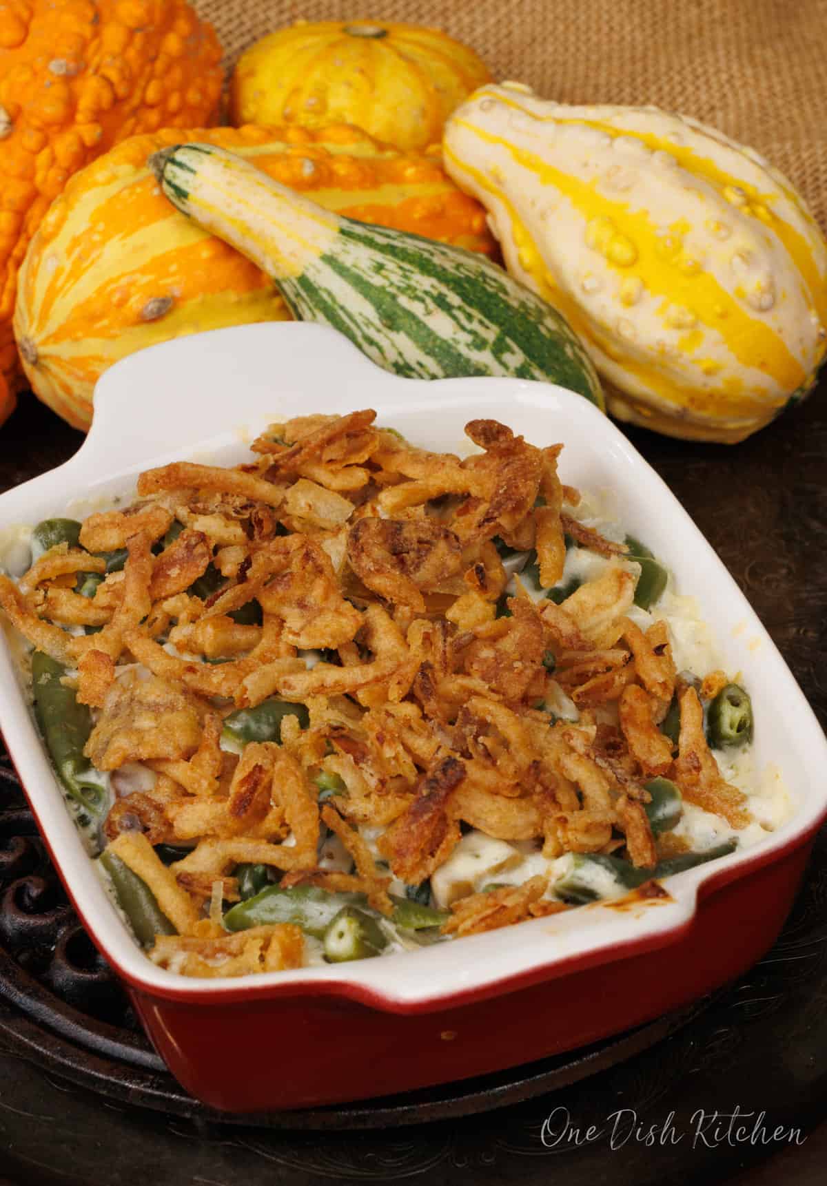 a small green bean casserole on a silver tray next to gourds