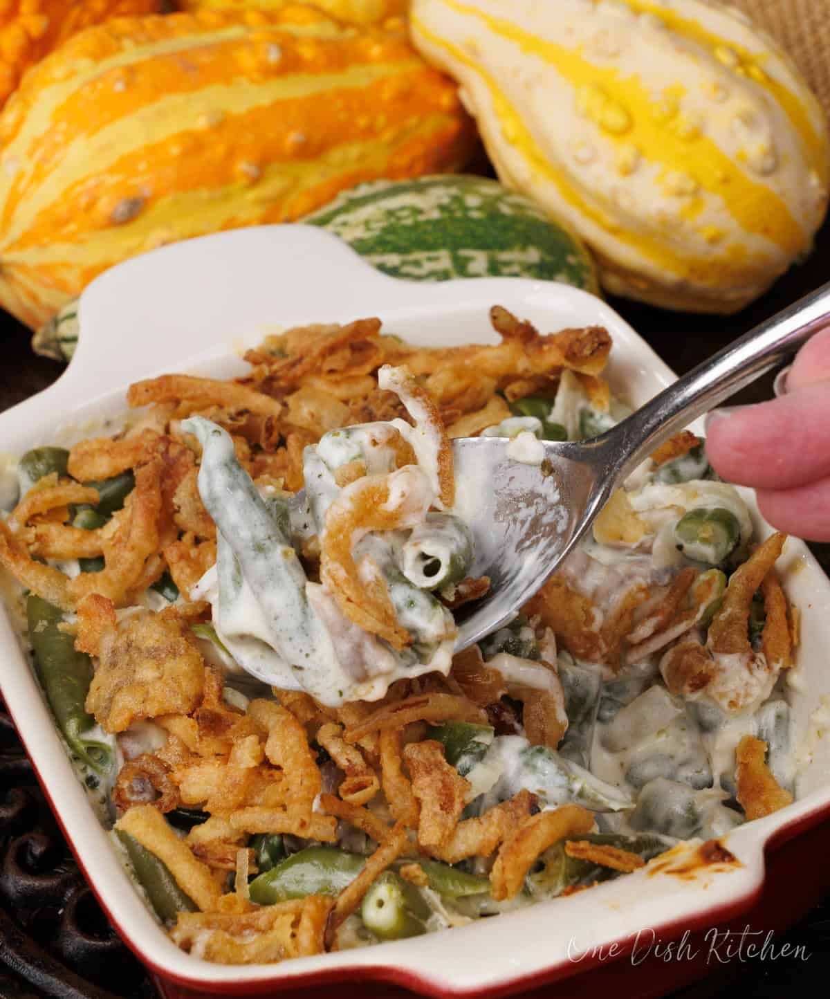 a spoonful of green bean casserole hovering above the small casserole dish