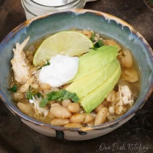 a bowl of white chicken chili topped with sour cream and avocado slices.