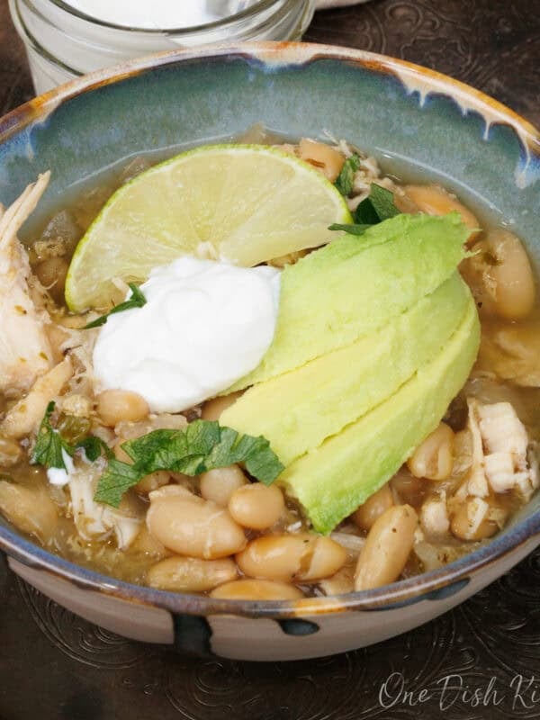 a bowl of white chicken chili topped with sour cream and avocado slices.
